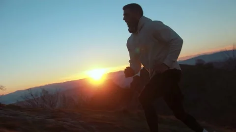 Young muscular man running through the beautiful landscape at sunset . Video stock 239556032
