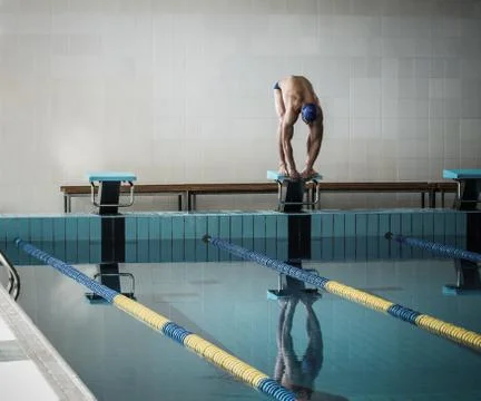 Young muscular swimmer in low position on starting block in a swimming pool Stock Photos