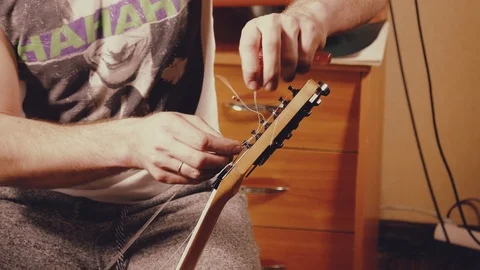 A young musician changes the strings on the guitar Stock Footage 103422898