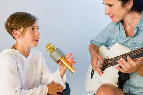 A young musician practices singing into a microphone while their instructor.. Stock Photos
