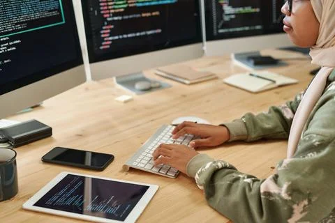 Young Muslim intern in hijab decoding data on computer screens by workplace Stock Photos
