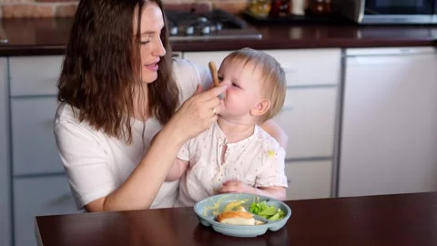 Young nanny sits at the table and spoon feeds the child healthy foods and Stock Footage 271067035