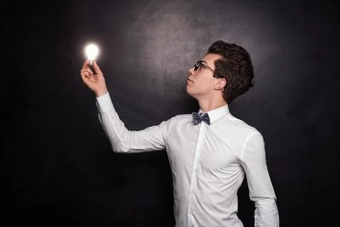Young nerd guy with bulb standing against black background Stock Photos