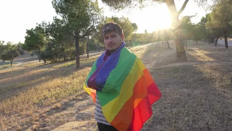 Young non-binary guy looking at camera wrapped in rainbow LGBTQ flag 스톡 동영상 250468800