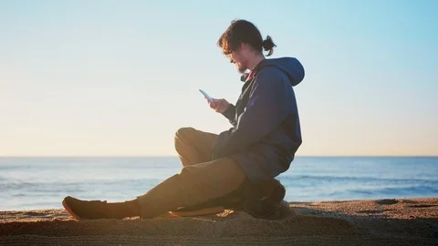 Young nostalgic man using mobile phone app connected to internet in sea beach Stock Footage 100896439