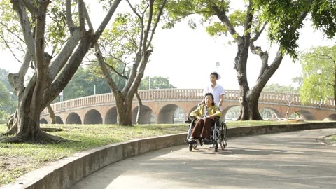Young nurse take caring old woman on wheelchair in the park Stock Footage 130104043