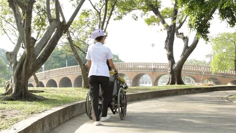 Young nurse take caring old woman on wheelchair in the park Stock Footage 130104151