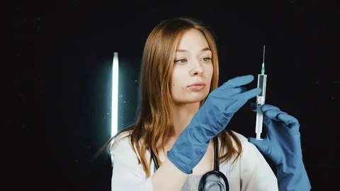 A young nurse will do an injection. She holds a syringe with an injection in her Stock Footage 90038787