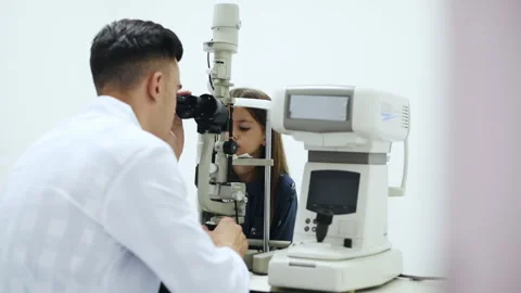 Young oculist in white coat using special device to check little girl's eye Video stock 304980643