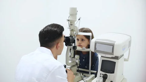 Young oculist in white coat using special device to check little girl's eye Stock Footage 304981089