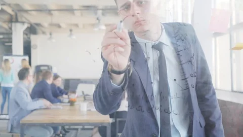 A young office employee writes formulas and graphs on a glass whiteboard using a Stock Footage 109566400