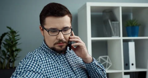 Young office manager in glasses with beard sits in modern office and talks on Stock Footage 147051807