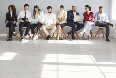 Young office people sits in queue waiting for job interview holding computer Stock Photos