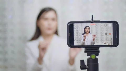 Young ophthalmologist doing live streaming via smart phone present new collec 스톡 동영상 188560229
