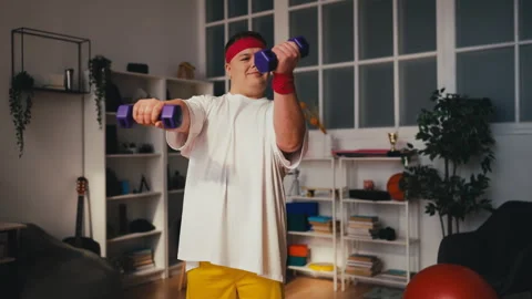 Young overweight man lifting dumbbells while training at home, burning calories Stock Footage 249210853