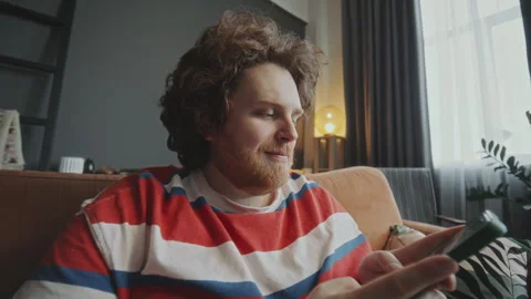 Young Overweight Man Sitting on Couch at Home and Using Smartphone Stock Footage 303208823