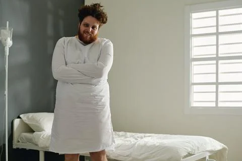 Young overweight man in white straitjacket standing by his bed in hospital ward Stock Photos