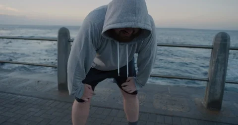 Young overweight runner man resting takes off hood exhausted after intense 库存影片 92772130