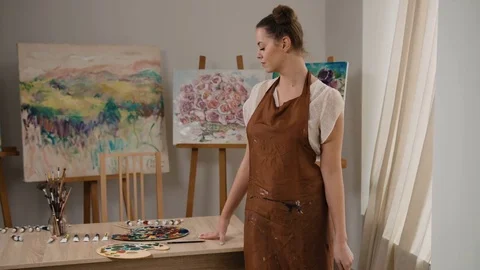 Young painter holding paintbrush in hand, posing with her masterpieces in art Stock Footage 74205919