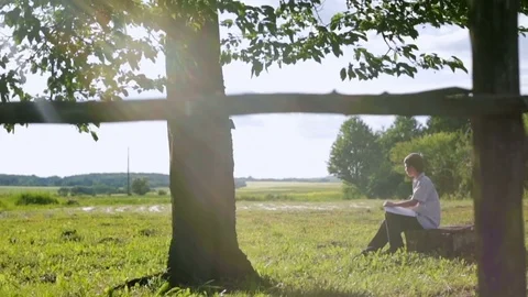 A young painter sitting under a tree paints a summer landscape Stockbeeldmateriaal 79382940