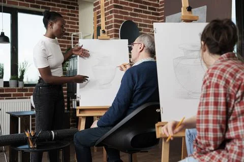 Young painter teacher explaining sketching technique to elderly student Stock Photos