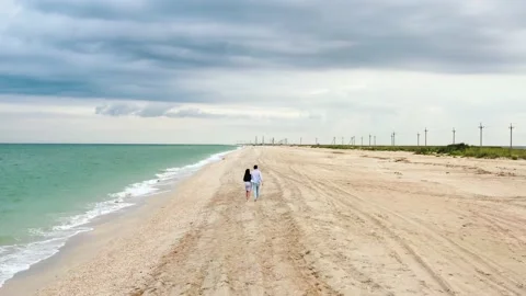 Young pair or couple of lovers hold hands and walk along the sand of a coastline Stock Footage 131521043