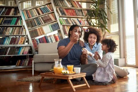 Young parents making soap bubbles and playing with their little daughter at h Stock Photos