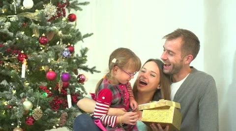 Young parents presenting a gift box to their daughter under a christmas tree Stock-Footage 50063382