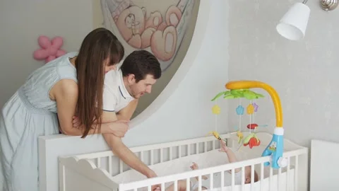 Young parents stand next to a crib looking at the baby Stock Footage 132006434