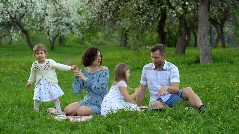 Young parents with two daughters spend leisure on a plaid in park on spring Stock Footage 109608167