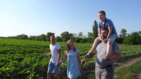 Young parents with two sons hold hands of each other walking along rural road Видео 337054568
