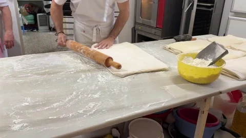 Young Pastry Chef Rolling Puff Pastry Dough on a White Marble Table Inside His Stock Footage 303338807