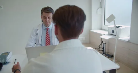 Young patient explaining health issues to his doctor who is working on lap top Stock Footage 270089933