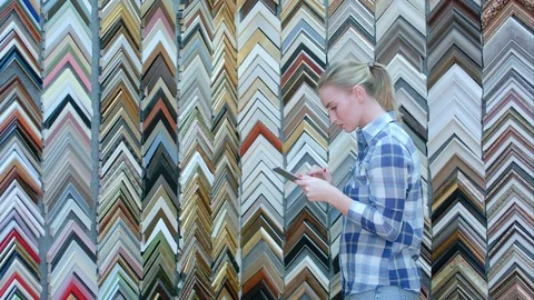 Young pensive female client looking for a frame, choosing, taking photo with Видео 75172397