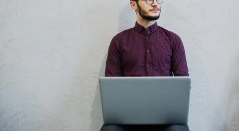 Young pensive guy using laptop, wearing glasses on background of white. Stock Photos