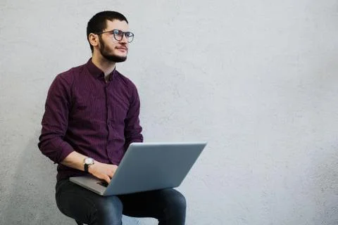 Young pensive guy using laptop, wearing glasses on background of white. Stock Photos