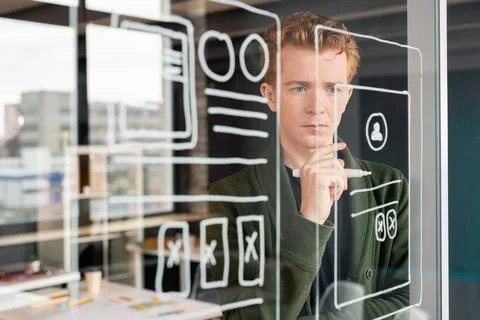 Young pensive male software developer looking at sketches of mobile application Foto stock