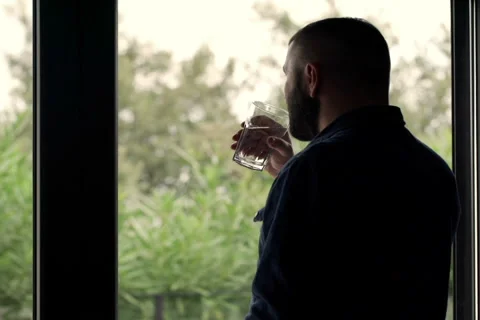 Young pensive man looking by the window and drinking water NTSC Stock Footage 57361149