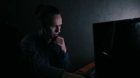 Young pensive man using computer at night in the dark room Видео 99051245