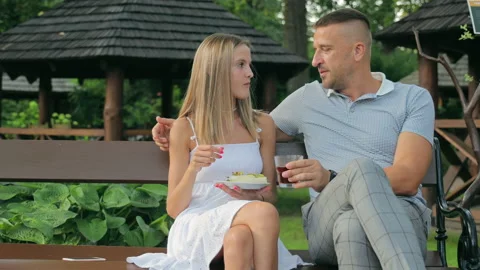 Young people are sitting on a bench and eating fruit. The girl does not let her Stock Footage 219670587