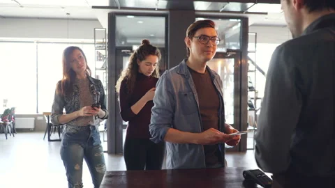 Young people are standing in line buying takeaway coffee and paying with mobile Stock Footage 89684262