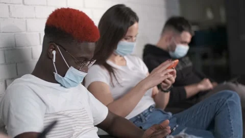 Young people of different races in protective masks sit on chairs in the Stock Footage 140992953