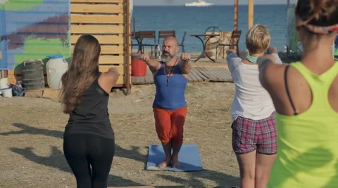 Young people doing sit-ups with a yoga teacher on the coast Stock Footage 60682341