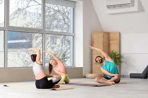 Young people with instructor practicing yoga in gym Stock Photos