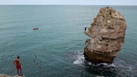 Young people jump into the sea from the sharp rocky cliffs at Tyulenovo Stock Footage 315414912