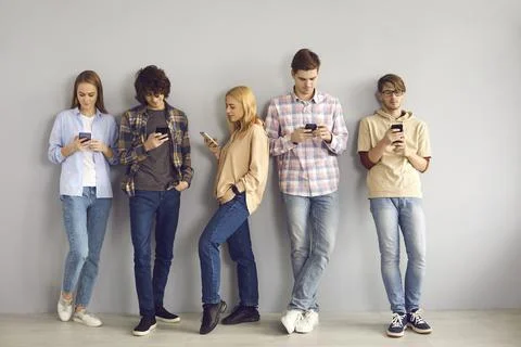Young people leaning on wall, using mobile phones and paying no attention to Foto stock