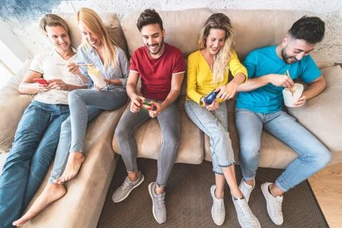 Young people playing console game while eating delivery asian food at home -  Stock Photos