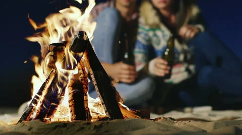 Young people relaxing by the fire, in the hands holding a bottle of beer or Stock Footage