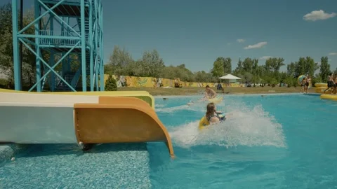 Young people roll down a yellow water slide in an aqua park. Stock Footage 299917118