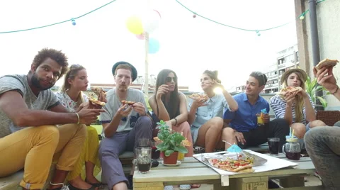 Young people sitting around the table and eating pizza on the rooftop terrace Stock Footage 68722640